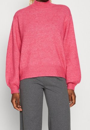 Růžový pletený rolák s dlouhými, vypouklými rukávy a žebrovanými manžetami a spodním lemem. Nosený s šedými úzkými kalhotami. Měkká textura, ležérní design.