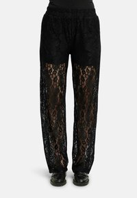 Juodos nėrinės kelnės su elastinga juosmens juosta, puoštos gėlių raštais ir permatomais intarpais, derinamos su juoda avalyne.