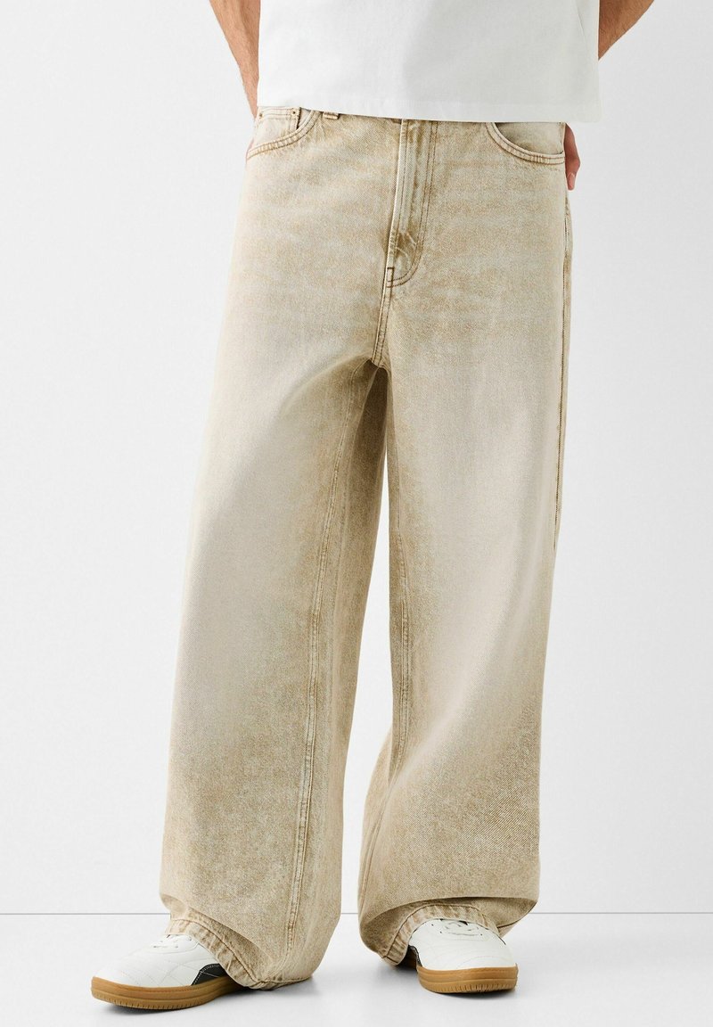 Beige vida byxor i denim med en urblekt textur, med kontrasterande sömmar och en klassisk femficksdesign.