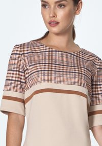 Beżowa sukienka z kratkowanym wzorem w ciepłych odcieniach, krótkie rękawy i poziome paski w kolorze brązowym na wysokości biustu. Miękka faktura materiału.