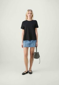 Svart bomull t-skjorte med korte ermer, parret med en slitt denimskjørt, flate sko med nagler, og en mønstret håndveske.