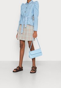 Veste en denim bleu clair avec manches bouffantes, taille ceinturée, mini-jupe à carreaux, sandales à lanières marron et sac à main texturé bleu clair.