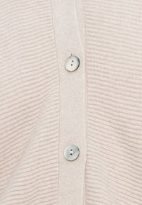 Cárdigan de punto acanalado en rosa claro con tres botones plateados redondos a lo largo de la tapeta, textura suave y un ajuste relajado.