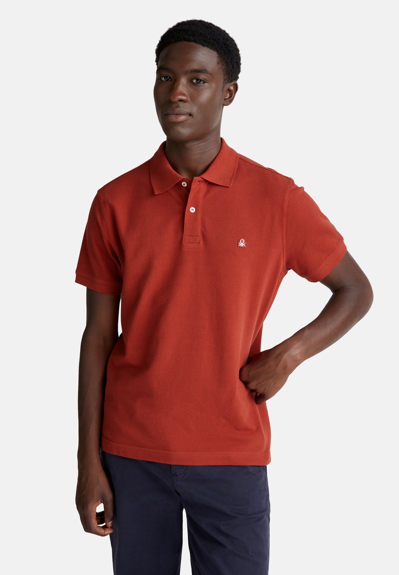 Polo a maniche corte di colore rosso mattone, realizzato in cotone, con colletto a 2 bottoni e piccolo logo sul petto. Tessuto morbido.