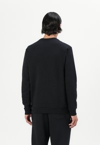 Sudadera negra de cuello redondo, mangas largas, puños y dobladillo de canalé, textura suave, diseño minimalista, combinada con pantalones negros a juego.