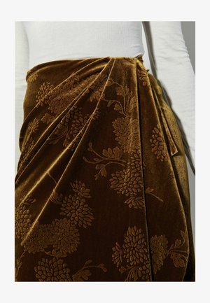 Brązowa aksamitna spódnica z kwiatowym wzorem, z koronkowym wykończeniem i miękką teksturą. Połączona z białą bluzką o prążkowanej strukturze.