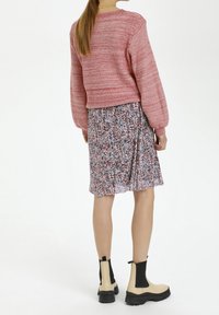 Pull en tricot rouge et rose, jupe à motifs floraux dans les teintes de rouge, noir et blanc, associée à des bottines beiges et noires.