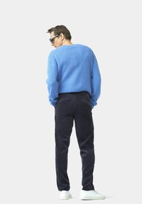 Hellblauer strukturierter Pullover, schwarze Cordhosen und weiße Sneakers, von hinten vor einem schlichten Hintergrund betrachtet.