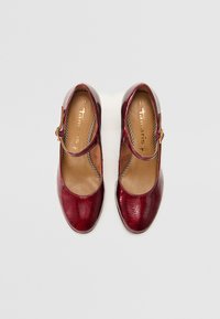 Chaussures en cuir rouge de style Mary Jane avec un bout rond, une sangle avec une quincaillerie en or et un dessus texturé. Taille 37 imprimée à l'intérieur.