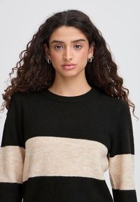 Jersey a rayas negro y crema con cuello redondo, mangas largas y una textura suave, que presenta una amplia franja crema en el pecho.