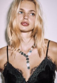 Silver-toned circular pendant necklace with varying sizes, worn over a black lace-trimmed fabric top with a V-neck design.