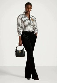 Cămașă călcată, albă cu dungi negre, cu un emblemă aurie, asortată cu pantaloni evazați negri din catifea și o mică geantă de mână neagră.