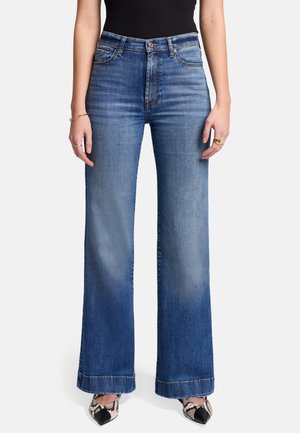 Hochtaillierte blaue Jeans mit weitem Bein, die einen verwaschenen Look und gesäumte Kanten aufweisen, kombiniert mit gemusterten Schuhen.