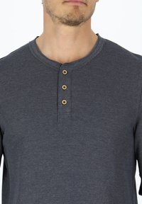 Mörkgrå långärmad henley-tröja tillverkad av texturerat material. Har en rundad halsringning och en placket med tre knappar i trä.