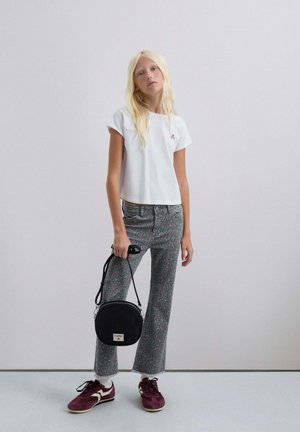 Camiseta corta blanca con un pequeño logotipo rosa, jeans acampanados grises con un patrón, bolso negro circular y zapatillas burdeos. Texturas suaves y estilo casual.