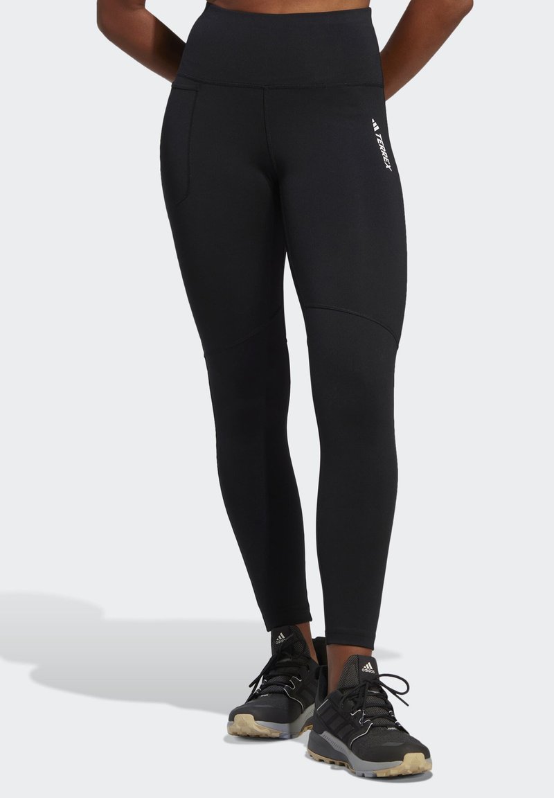 Sorte træningsleggings med høj talje, sidelommer og en glat tekstur. Har elegante linjer og mærkeaccenter på siden.