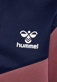 Valkoinen hummel-logo tyylitellyllä ampiaisella tekstin yläpuolella tummansinisellä ja viininpunaisella kankaalla, jossa on diagonaalinen värijako.