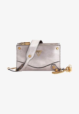 Pochette Guess argentée avec clous dorés, plaque logo, sangle épaisse, fermeture éclair et chaîne dorée décorative avec breloque cadenas.