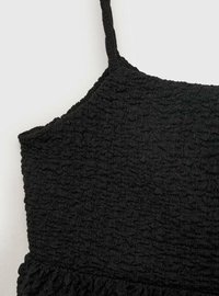 Top negru dintr-un material texturat, cu bretele subțiri și un tiv volanat. Textura are un aspect șifonat și adunat.