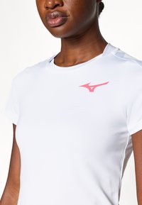 Valge sportlik t-särk lühikeste varrukatega, mille ülemisel vasakul küljeal on roosa logo ning sile ja kerge kangas.