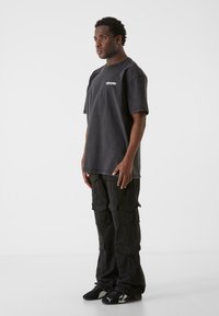 Sort oversized t-shirt med hvidt logo på brystet, parret med sorte cargo-bukser der har flere lommer og en afslappet pasform.