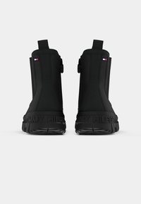 Bottines noires à finition lisse, avec une petite patch logo et une semelle texturée, conçues pour le confort et la durabilité.