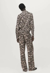 Majica z dolgimi rokavi in ujemajoče hlače s temno rjavo osnovo, okrašeni s kontrastnim svetlo bež in roza abstraktnim vzorcem.