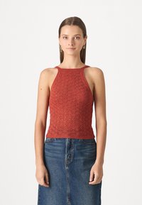 Haut halter tricoté rouge avec un motif en losange, doté d'un col et de bras côtelés, associé à une jupe en denim.