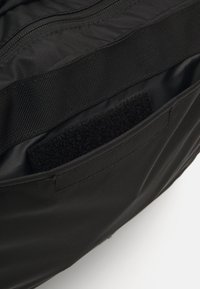Interior de uma bolsa de tecido preto com um compartimento com fecho, um patch de velcro e forro texturizado para organização.