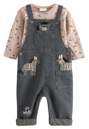 Chemise beige à manches longues pour enfant avec motifs noirs sous une salopette gris foncé avec des écussons zèbre et le texte "Go Wild" sur une jambe.