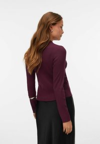 Raštuota bordo spalvos palaidinė ilgomis rankovėmis ir aptemptu fasonu. Savybė yra banguotos apdailos apačia ir lygi tekstūra, derinama su elegantišku juodu sijonu.