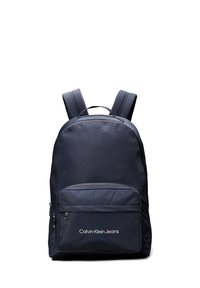 Zaino blu navy realizzato in tessuto liscio, dotato di spallacci imbottiti, una tasca frontale con zip e il logo "Calvin Klein Jeans" sulla parte anteriore.