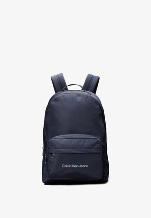 Zaino blu navy realizzato in tessuto liscio, dotato di spallacci imbottiti, una tasca frontale con zip e il logo "Calvin Klein Jeans" sulla parte anteriore.