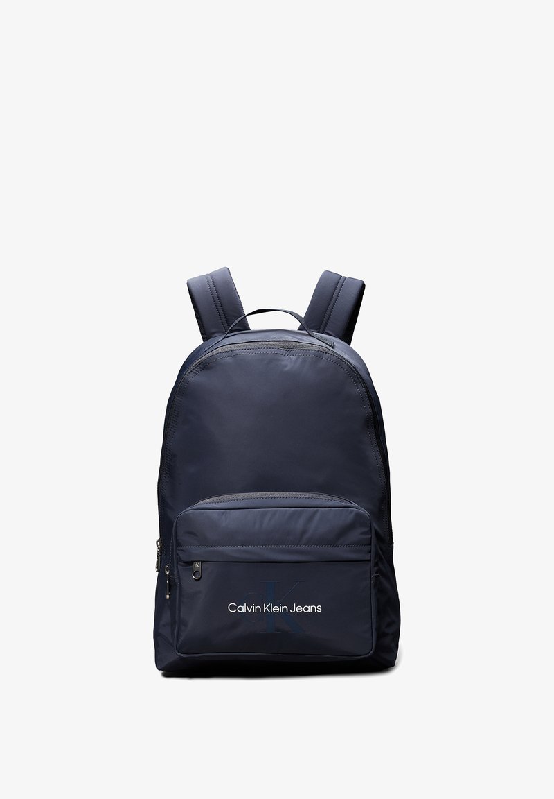 Zaino blu navy realizzato in tessuto liscio, dotato di spallacci imbottiti, una tasca frontale con zip e il logo "Calvin Klein Jeans" sulla parte anteriore.