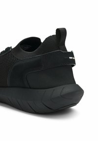 Black athletic shoe with mesh upper, padded heel, pull tab, and thick textured sole, shown from rear side angle.