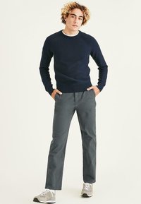 Pull en tricot marine, pantalon en coton gris et baskets gris clair. Le pull a un col rond et des poignets côtelés, le pantalon présente une coupe décontractée.