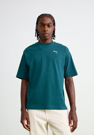 Teal bomulds T-shirt med korte ærmer, rund halsudskæring og lille hvid Puma-logo på brystet. Sammen med lyse stribede bukser.
