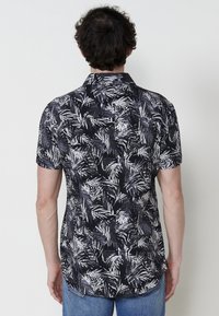 Camisa de manga corta en negro con un patrón de hojas blancas, con un cuello clásico y un corte relajado, hecha de una tela ligera.
