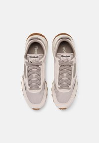 Ljusgrå sneakers med ovandel i nät och mocka, med beige detaljer och en brun gummisula. Snörning och varumärkeslogotyp på tungan.