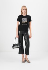 Black t-shirt with leopard print graphic and "future" text, paired with black faux leather wide-leg pants and taupe heels, holding a black handbag.
