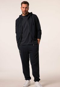 Navy hoodie and sweatpants set made of soft fabric, featuring a zip, round neckline, and printed logo accents. Paired with white sneakers.