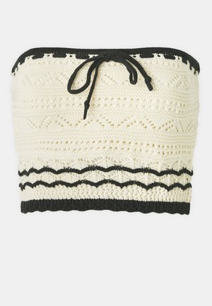 Pletený crop top v slonovinovej farbe s texturovaným vzorom, s čiernym elastickým pásom na vrchu a na spodku a s detailom viazania vpredu.