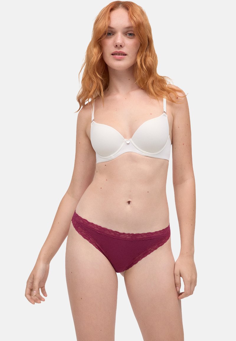 Sostén blanco acolchado con tirantes ajustables y un pequeño lazo en el frente. Tanga burdeos con encaje. Tela suave, diseño ajustado.