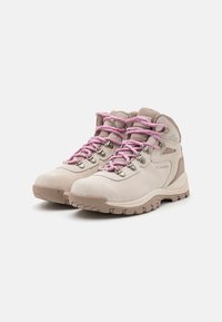 Bottes de randonnée beige clair avec des lacets roses et des œillets métalliques, dotées d'une tige texturée et d'une semelle extérieure en caoutchouc durable pour une meilleure adhérence.