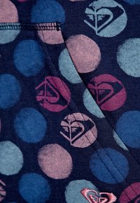 Tissu foncé avec de grands pois bleu, rose et bleu clair. Certains pois présentent des logos stylisés dans des couleurs contrastées. Texture douce.