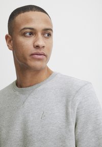 Gray sweatshirt with a round neckline, textured fabric, and a small embroidered logo on the chest. Features subtle stitching details.