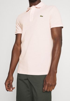 Polo en coton rose clair avec un col classique, des manches courtes et un logo brodé vert sur la poitrine à gauche.