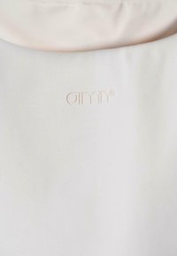 Felpa beige chiaro con una texture liscia, caratterizzata da un piccolo logo a rilievo di un colore abbinato e discreto vicino al colletto.