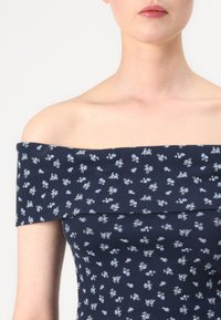 Marineblå avdempet kjole med ribbet tekstur, prydet med små lyseblå blomstermønstre over stoffet og bred halsutringning.