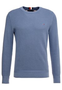 Blå stickad tröja med ett strukturerat mönster, rund hals och ribbade ärmslut. Har en liten logotyp med röda och mörkblå ränder vid halslinningen.